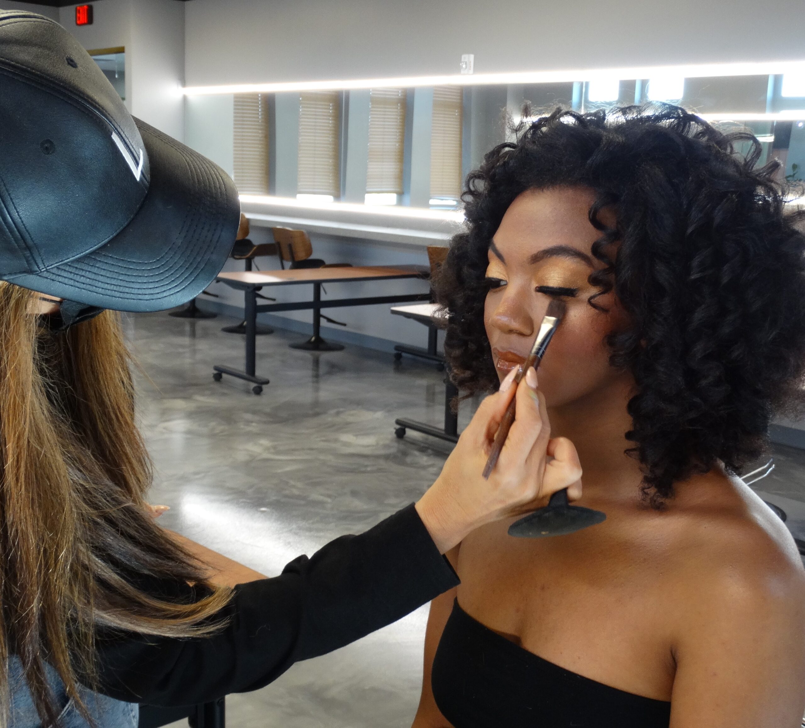 Makeup class at L Makeup Institute with student practicing professional beauty techniques on model, focusing on complexion and highlight application in a classroom setting
